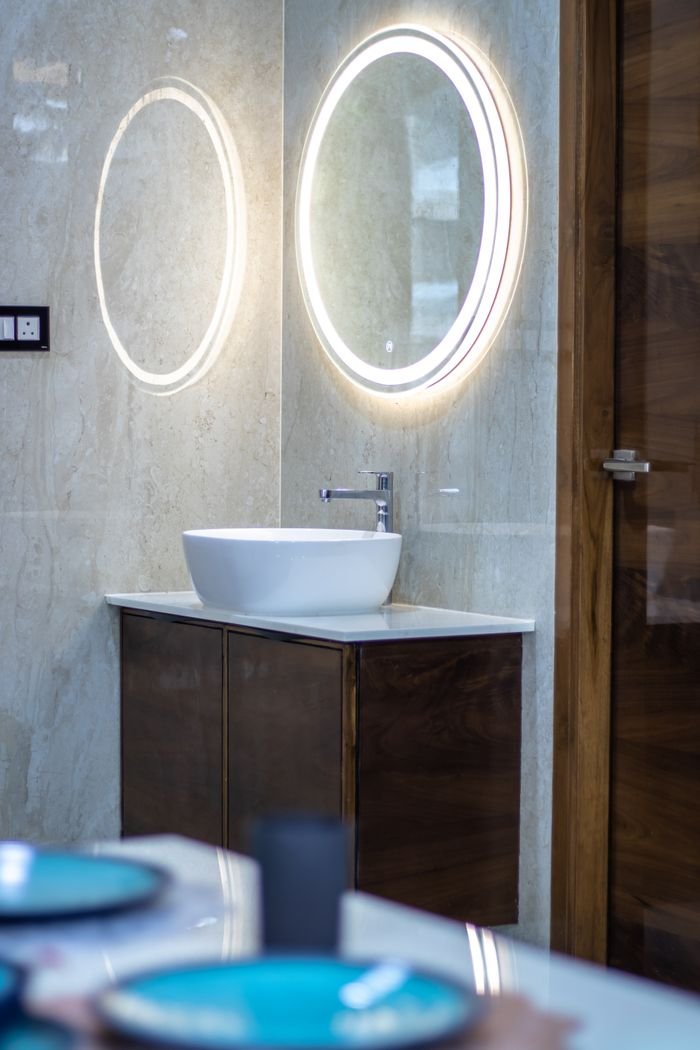 Contemporary bathroom featuring an illuminated round mirror, sleek sink, and wooden accents.